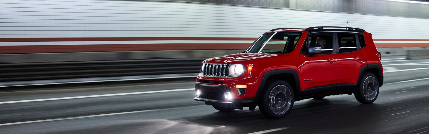 A red 2021 Jeep Renegade being driven through a tunnel with headlamps lit.